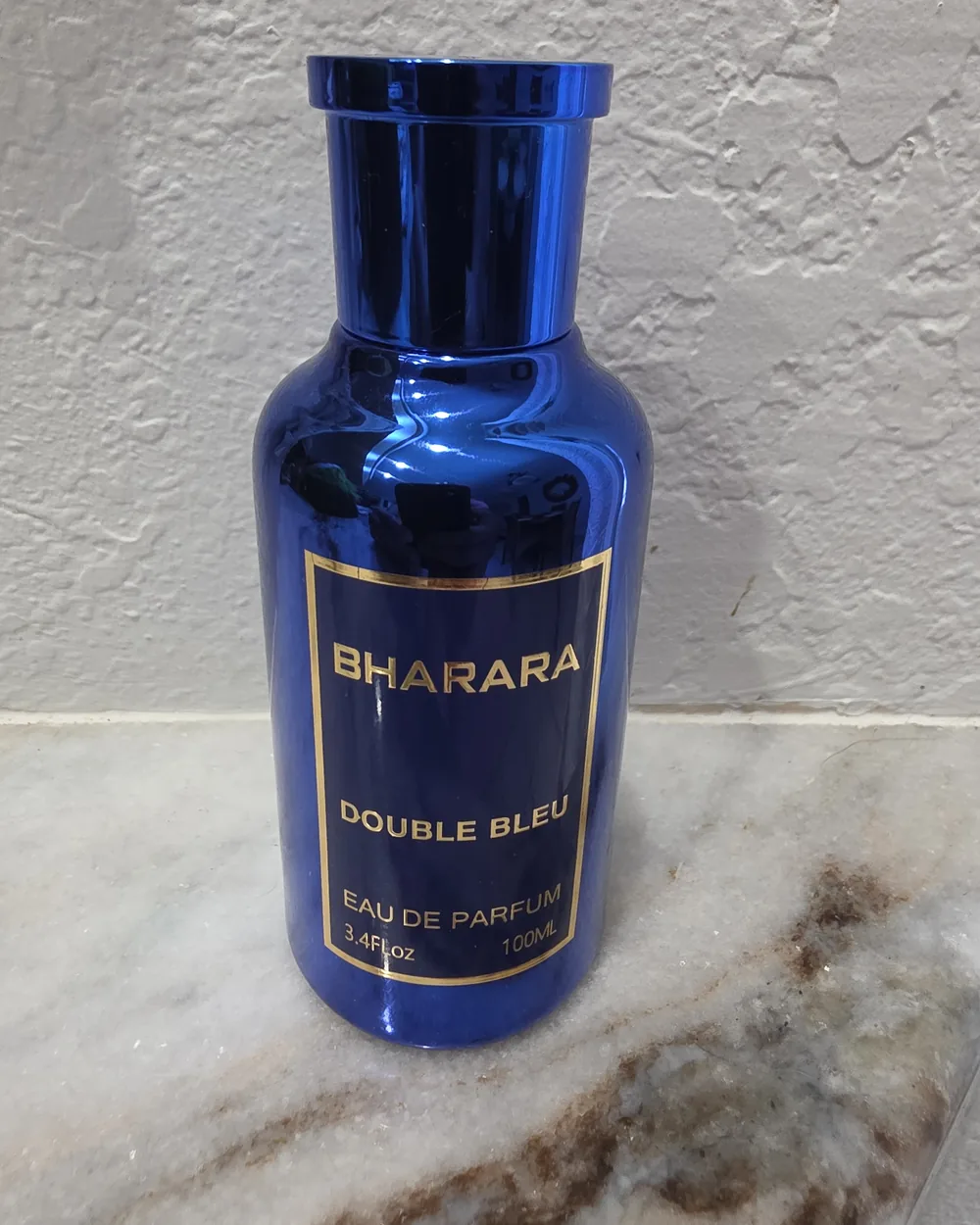 Before: a phone photo of a blue Bharara Double Bleu eau de parfum bottle on a marble countertop against a textured white wall